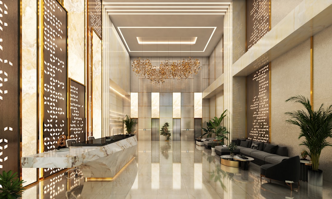 Elegant, high-end lobby with marble reception desk, modern furnishings, and intricate gold accents. The space features dramatic lighting, high ceilings, and lush greenery, creating a luxurious and welcoming atmosphere.